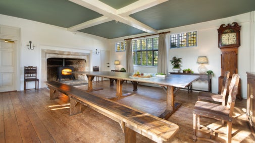 The dining room at Thorington Hall with long wooden table, benches, chairs and fireplace with woodburner, Suffolk